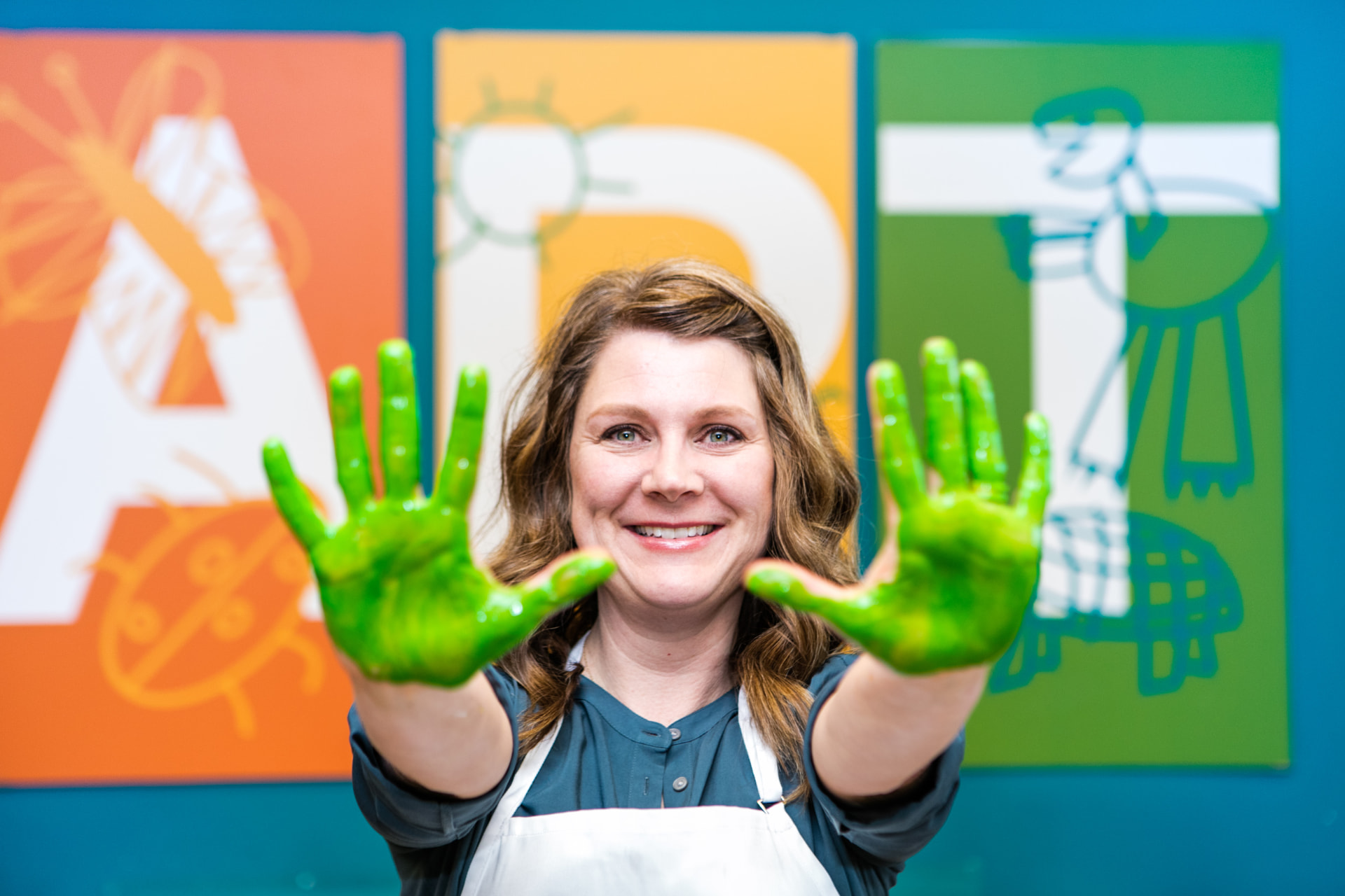 A Kidcreate Studio owner smiling in her studio with green paint on her hands