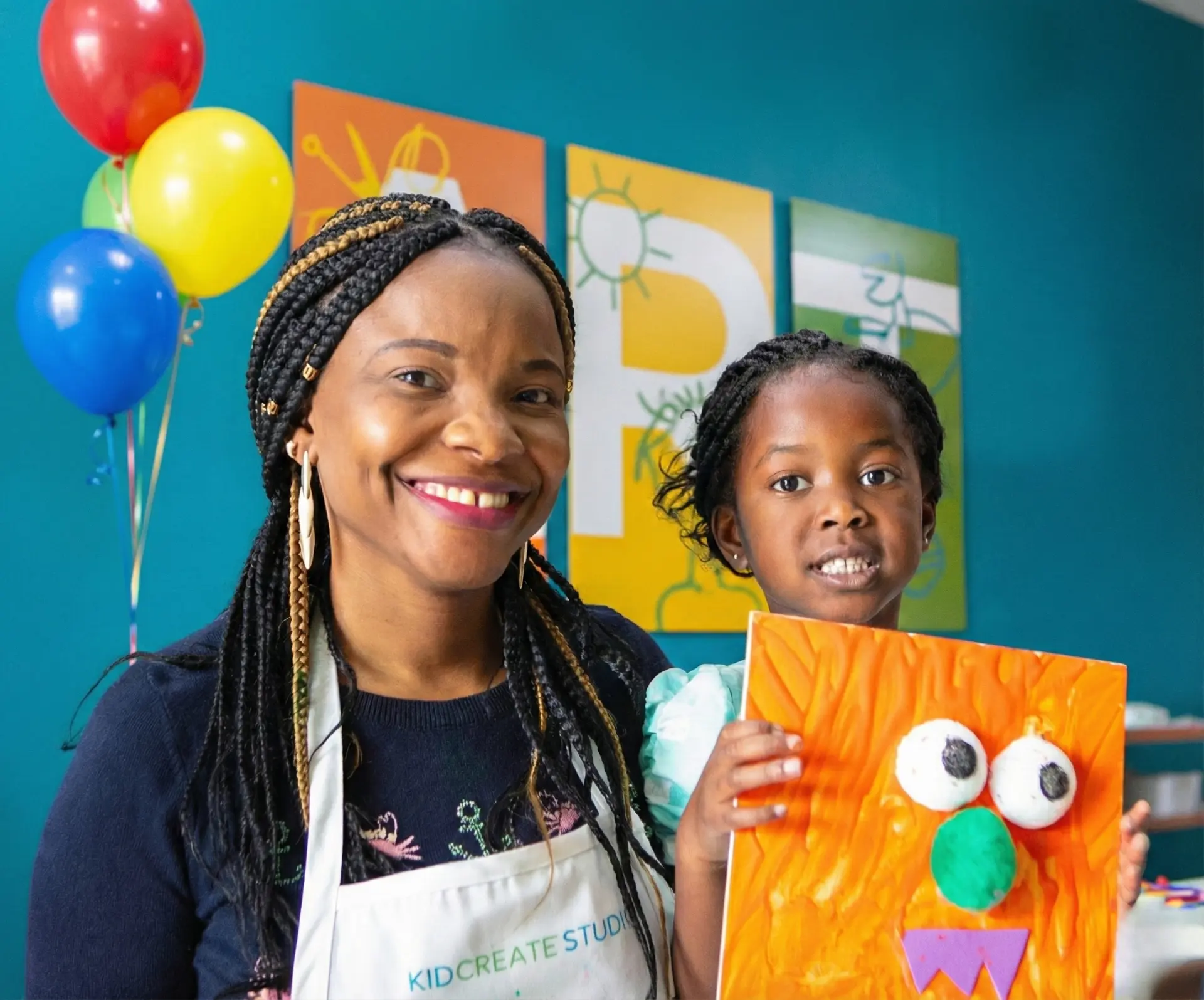 A parent and child holding up a mixed-media art project together at a Kidcreate birthday party